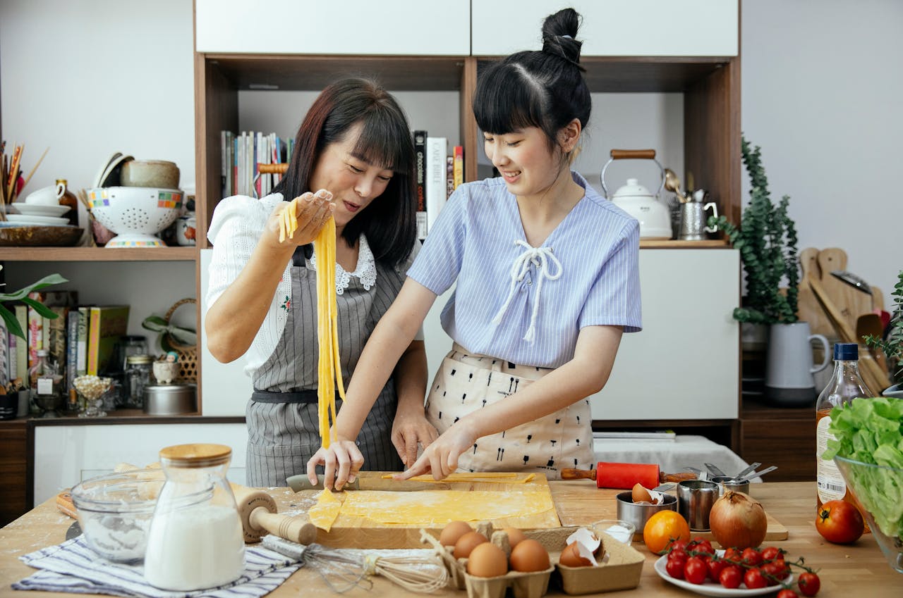 A joyful mother and daughter prepare homemade pasta together in the kitchen.